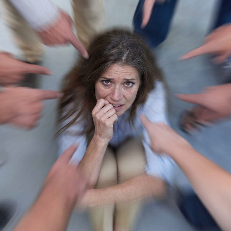 Femme d'âge mûr exprimant l'angoisse liée à la blemmophobie et le besoin de s’affranchir du regard des autres, entourée de mains accusatrices pointées vers elle.